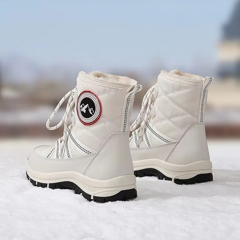 A pair of off-white quilted winter boots with black soles, shown standing on snow with a blurred outdoor background.