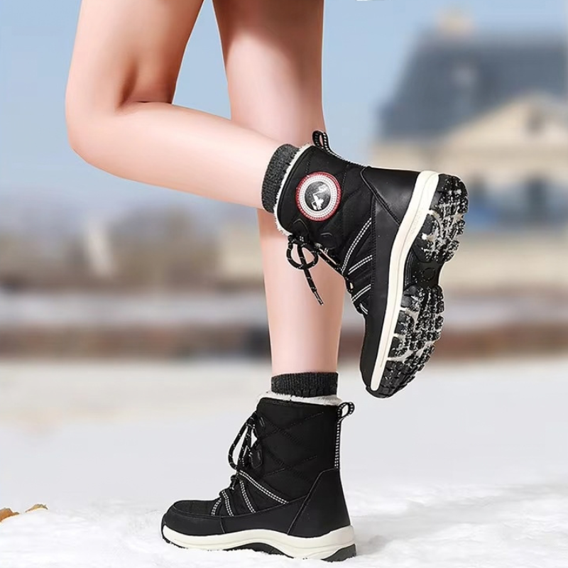 Black mid-calf winter boots with white soles and black socks, shown on a person's legs standing in snow outdoors.
