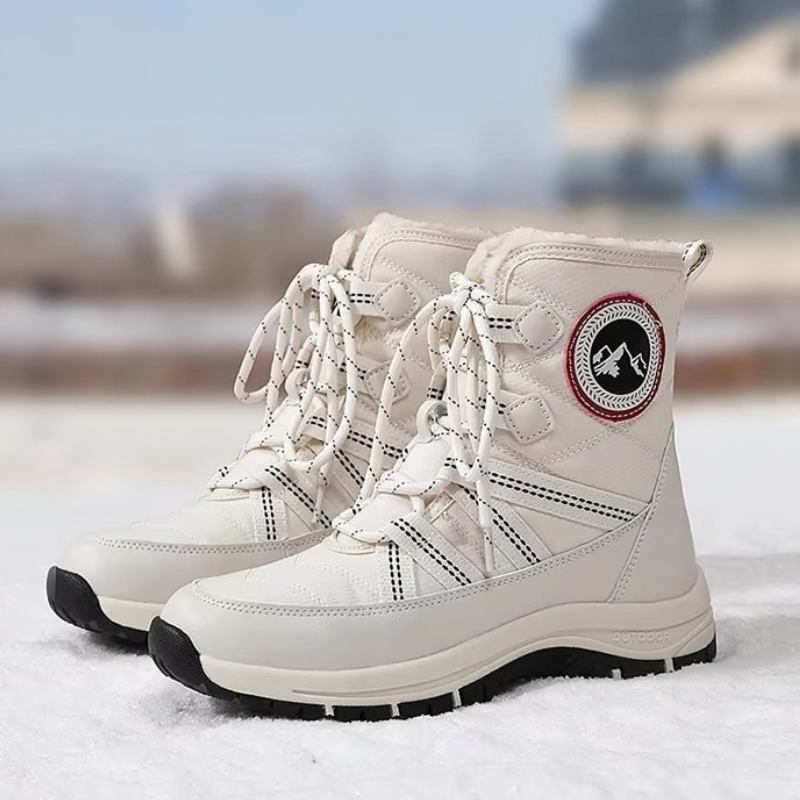 A pair of off-white high-top winter boots with black soles, shown standing on snow with a blurred outdoor background.