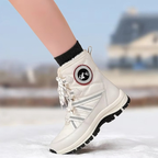 A person's leg wearing a white mid-calf winter boot with a black sock, standing on snow with a blurred outdoor background.