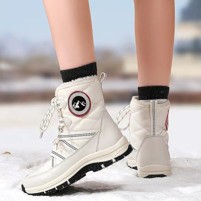 A pair of off-white winter snow boots with black soles and black socks, shown on a person's feet standing in snow.