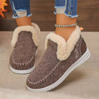 Brown fuzzy boots with white soles worn by a person on a beige surface.
