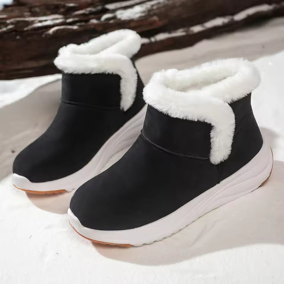 A pair of black mid-calf winter boots with white faux-fur trim and thick white soles, photographed on a snowy surface with a dark log in the background.