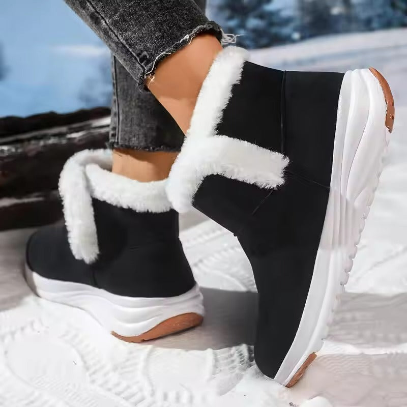 A person wearing black winter ankle boots with thick white faux-fur trim and chunky white soles, standing outdoors on snow.