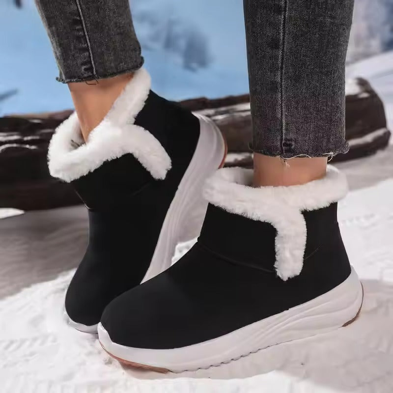 A person wearing black mid-calf winter boots with white faux-fur trim and thick white platform soles, standing in a snowy outdoor setting.