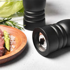 Black pepper grinder next to a plate of food on a light surface