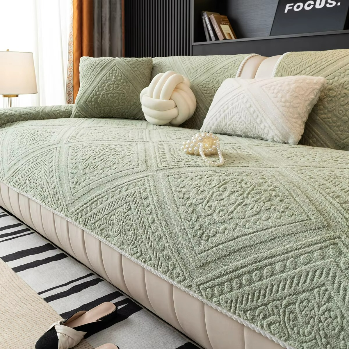 Green textured sofa cover on a sofa with decorative pillows in a living room setting.