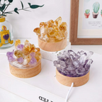 Three crystal arrangements in wooden bases on a white surface with a plant and framed picture in the background.