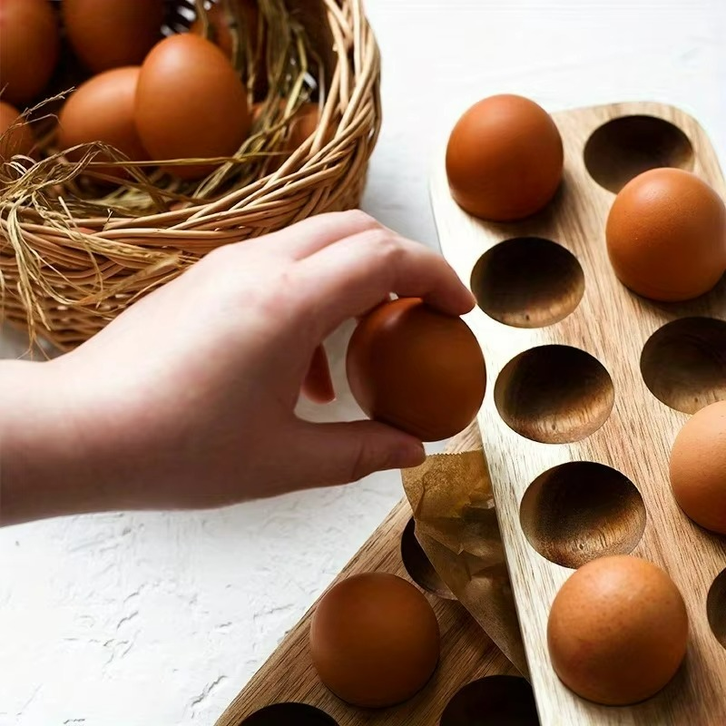 Hand placing eggs into a wooden egg holder with a basket of eggs in the background.