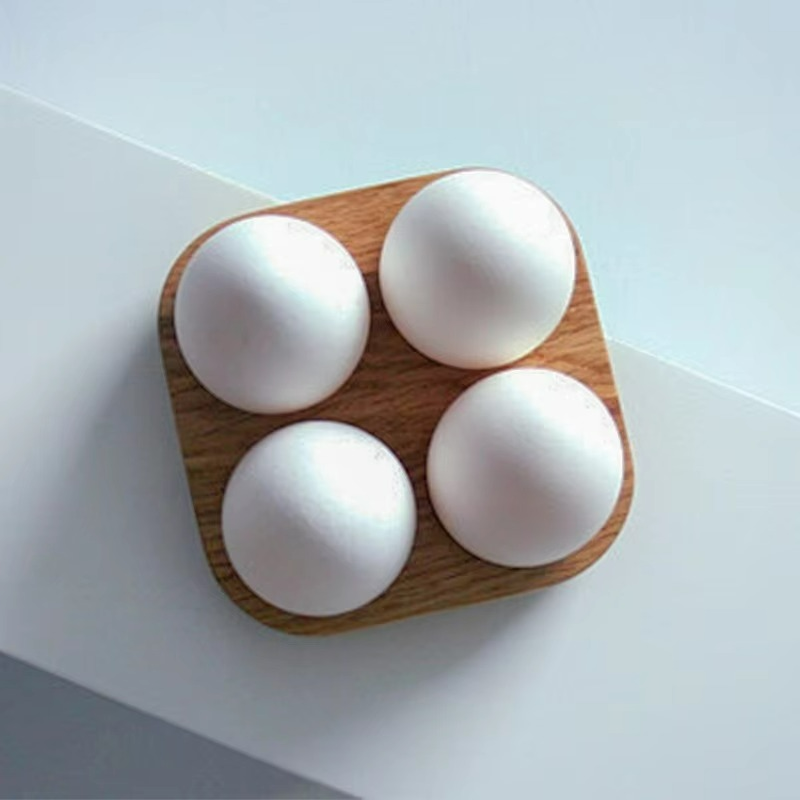 Four white eggs on a wooden tray with a light gray background