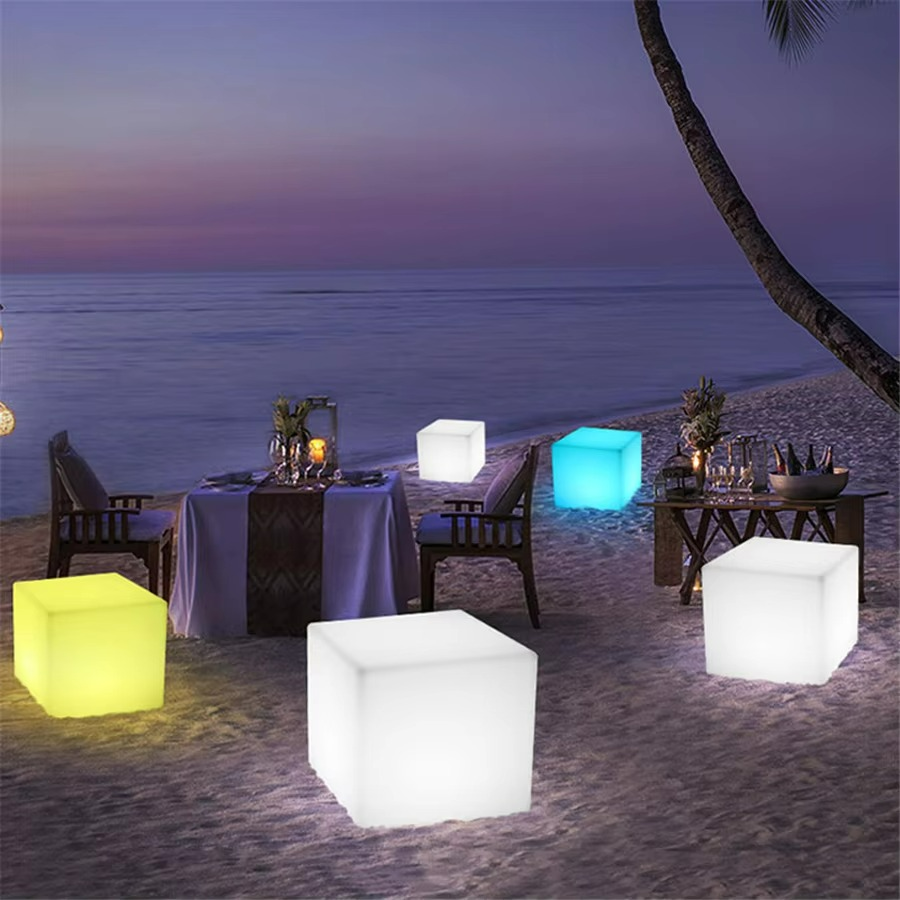 Glowing cube lights on a beach at night with tables and chairs.
