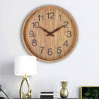 Wooden wall clock on a white wall with a lamp and decorative items below.