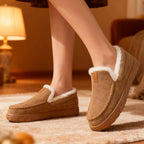 Brown slippers with white fur lining worn indoors on a carpeted floor.