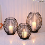 Three black wire candle holders with candles inside on a white surface.