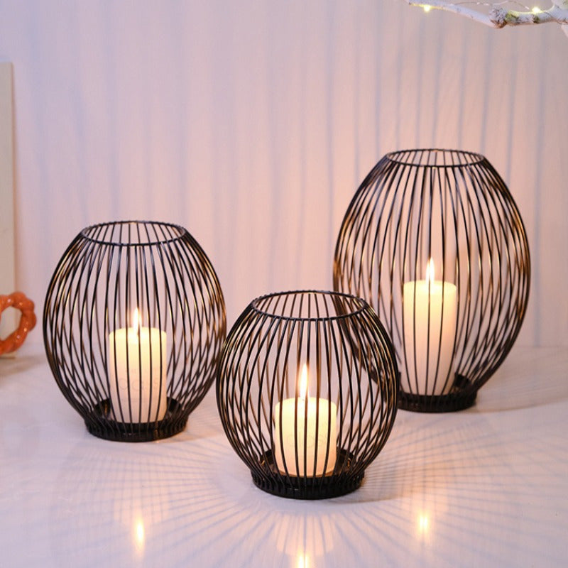 Three black wire candle holders with candles inside on a white surface.