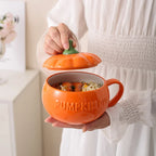 Person holding an orange pumpkin-shaped mug with a lid, filled with food.