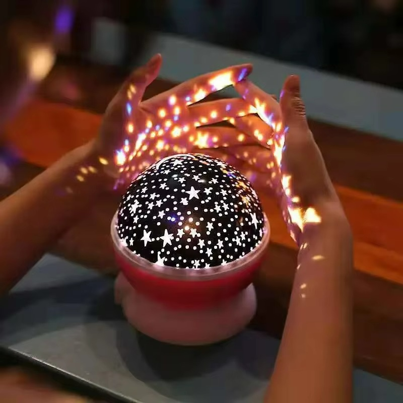 Starry night light projector with hands holding it, creating star patterns on a blurred background