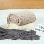 Folded beige and gray blanket on a bed with a wooden headboard.