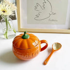 Pumpkin-shaped teapot with a matching spoon on a table with a framed picture in the background.