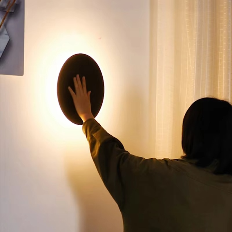 Person adjusting a wall-mounted lamp in a room with curtains.