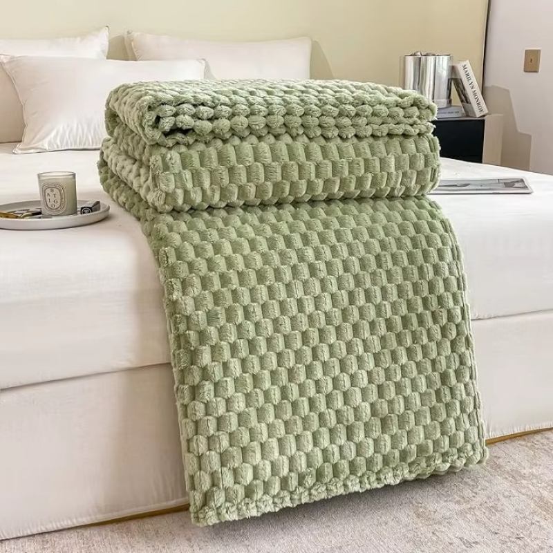 Green textured blanket draped over a white sofa in a living room setting.