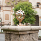 Decorative gold sphere on a stone pedestal with a blurred building and trees in the background
