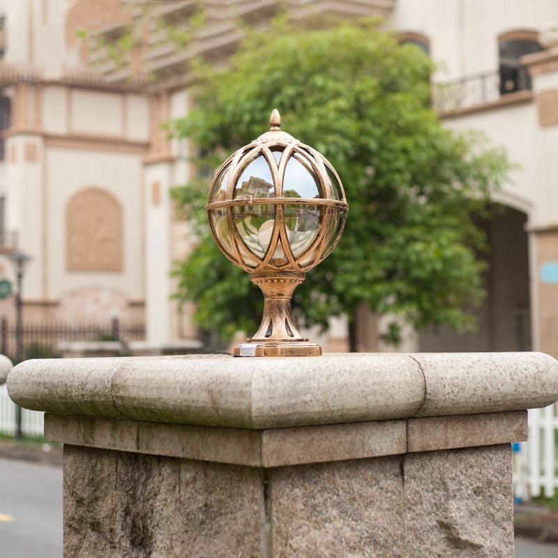 Decorative gold sphere on a stone pedestal with a blurred building and trees in the background