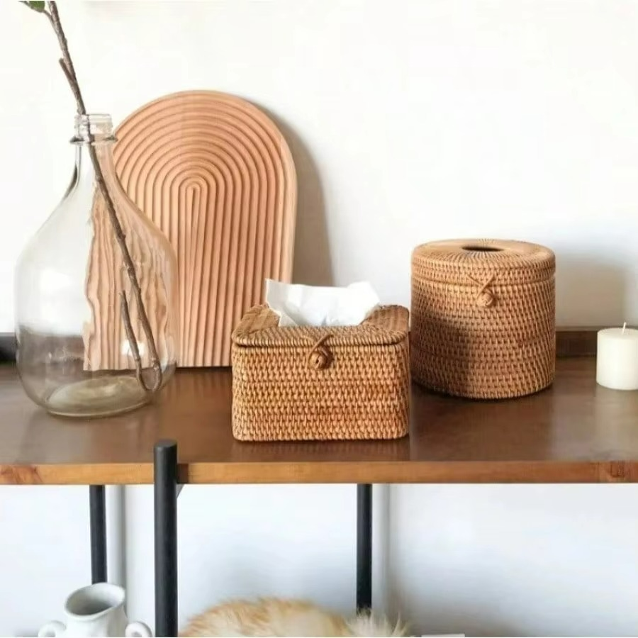 Woven baskets and a glass vase on a wooden surface with a white wall background
