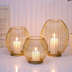 Three gold wire candle holders with candles on a textured surface.