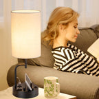 Woman sitting on a couch with a lamp, phone, and mug on a table next to her.