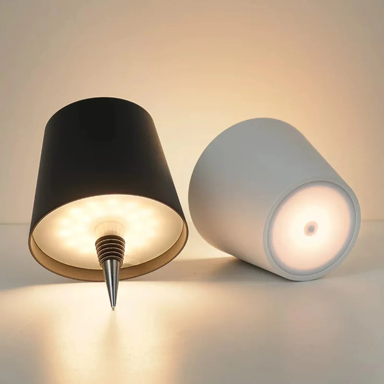 Two cylindrical lamps, one black and one white, on a neutral background.