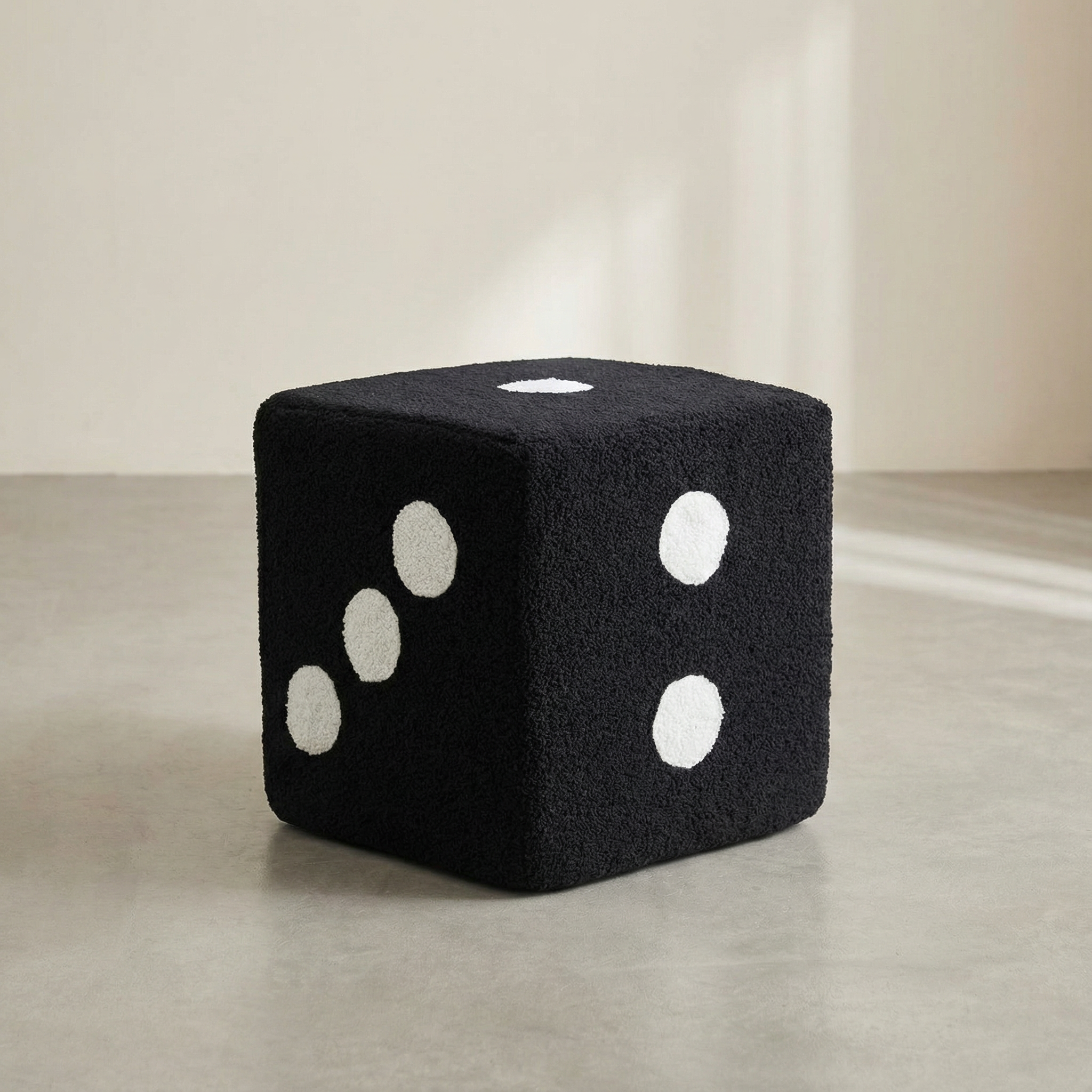 Black cube-shaped ottoman with white dots on a neutral background