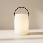 Modern lantern-style lamp with a black handle on a neutral background