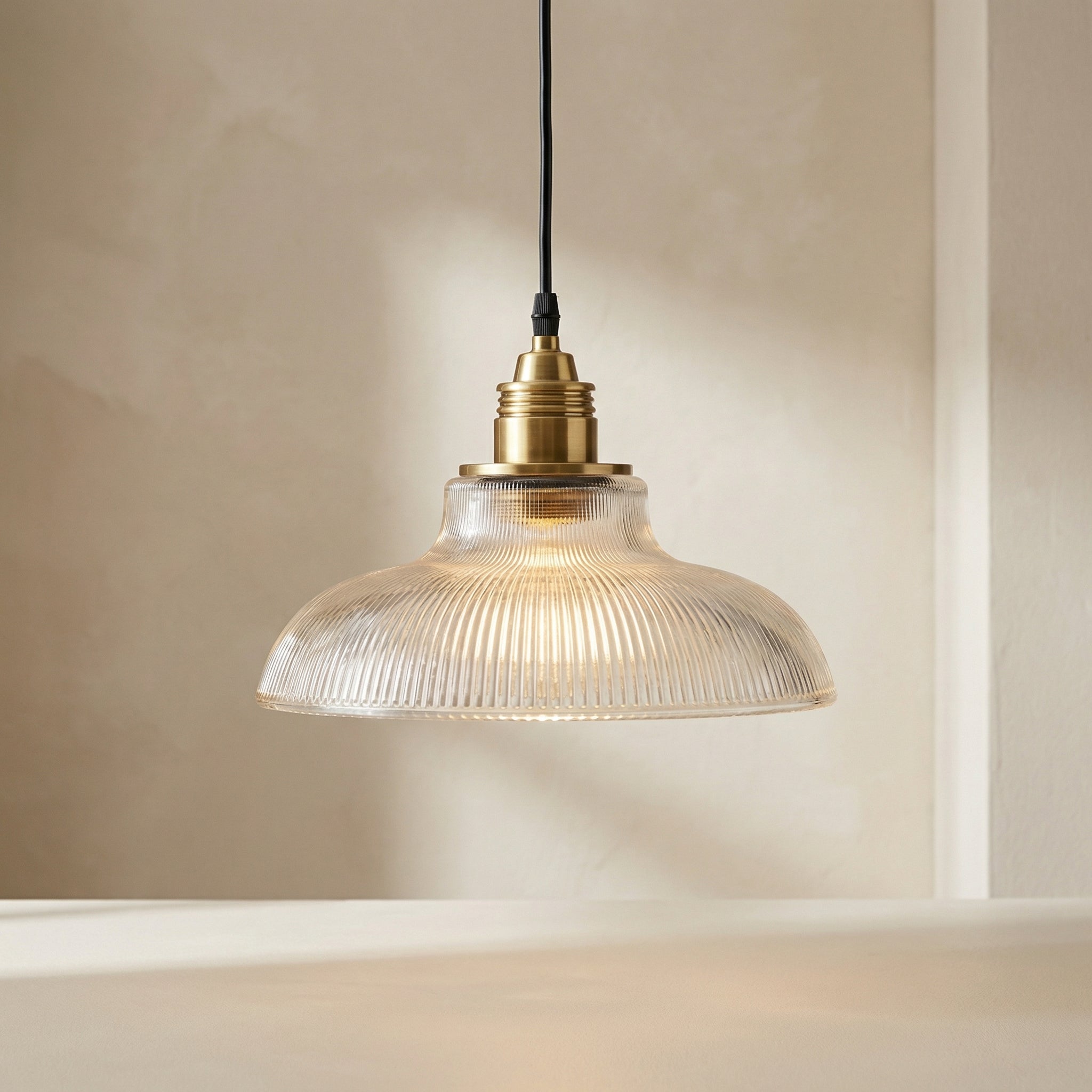 Pendant light with glass shade and brass fitting on a neutral background
