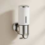 Wall-mounted soap dispenser with white and chrome finish on a beige wall.
