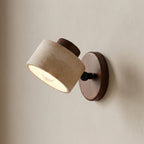 Wall-mounted light fixture with beige shade and wooden base on a neutral wall.