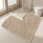 Beige bath mat on a bathroom floor with a shower and toilet in the background.