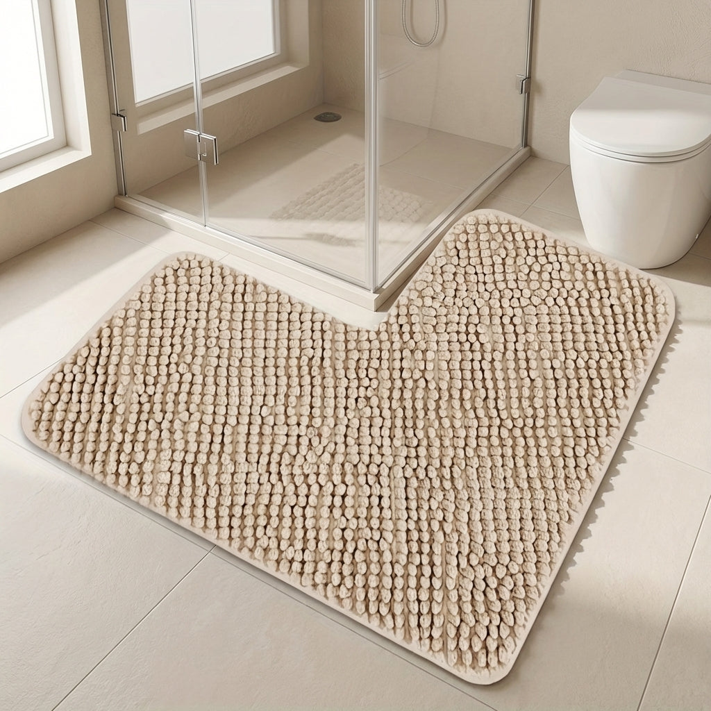 Beige bath mat on a bathroom floor with a shower and toilet in the background.