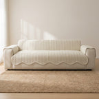 Beige sofa with a striped cover in a minimalistic room with a beige wall and wooden floor.