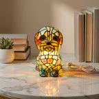 Colorful stained glass dog-shaped lamp on a marble surface with books and a plant in the background.