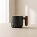 Black ceramic mug with wooden handle on a beige surface