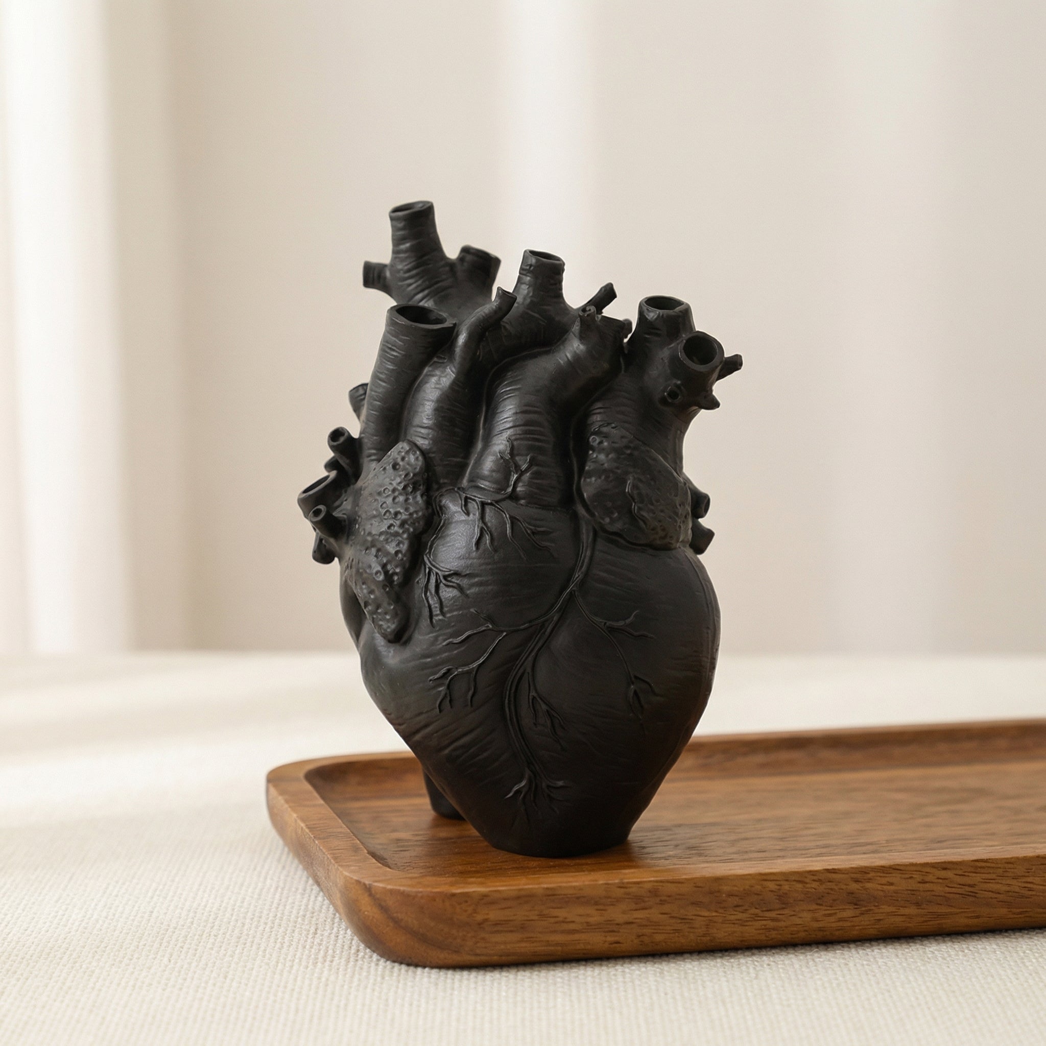 Black ceramic heart-shaped vase on a wooden tray with a beige background