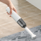 Hand holding a white handheld vacuum cleaner on a wooden floor.