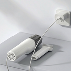 Hair dryer with attachments plugged into a wall socket on a white surface.