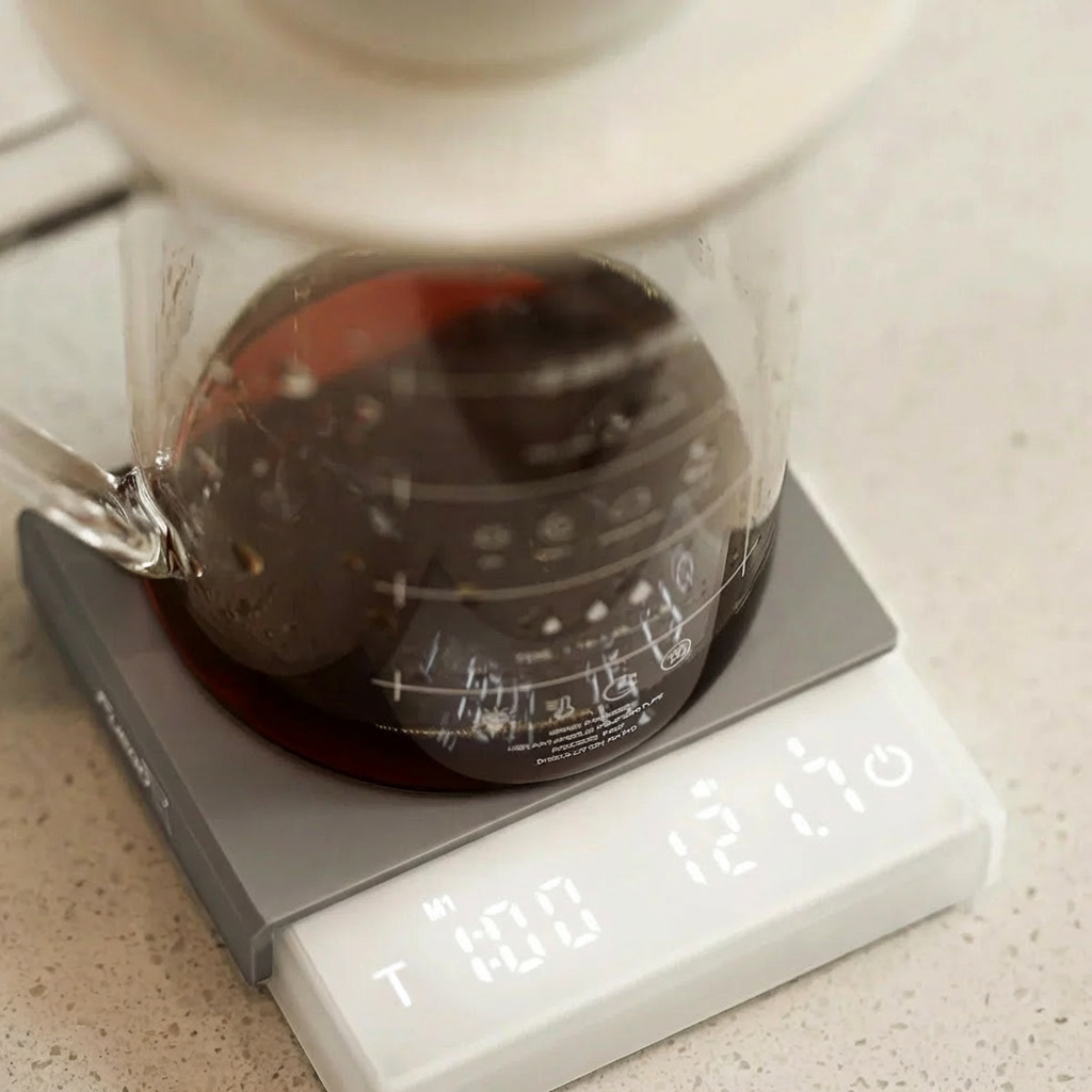 Coffee maker with a glass carafe on a digital scale displaying weight.