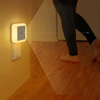 Person walking towards a wall-mounted night light in a dimly lit room.
