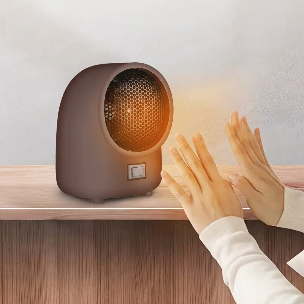 Small round heater on a wooden surface with hands warming up next to it.