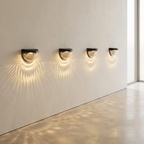 Four wall-mounted lights casting shadows on a light-colored wall.
