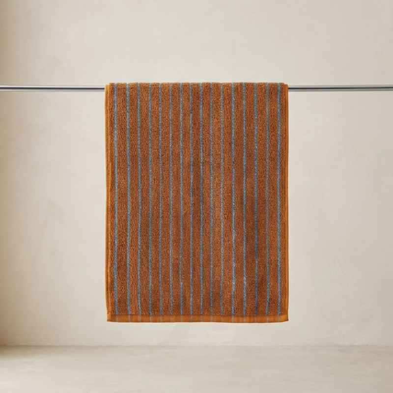 Brown striped towel hanging on a silver rack against a beige wall.