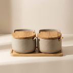 Two ceramic containers with wooden lids on a matching wooden tray against a beige background